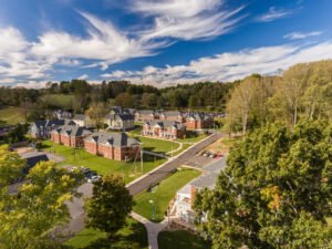Aerial drone photograph of the Emory & Henry College student village showing multi-story brick residence buildings, tree-lined access roads, and green campus quads beneath dramatic wispy cirrus clouds.
