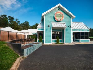 Commercial exterior architectural photograph of Aretha Frankensteins restaurant showing turquoise horizontal siding, round logo sign, metal roofing, corrugated planter boxes, and umbrella dining patio by Dwayne Hickson, Graphic Productions in Pigeon Forge, TN.