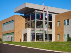 Exterior commercial architectural photograph of the Emergency Response Training Facility main entrance featuring a cantilevered metal roof canopy, glass curtain wall atrium, and flagpoles by Dwayne Hickson, Graphic Productions in Oak Ridge, TN.