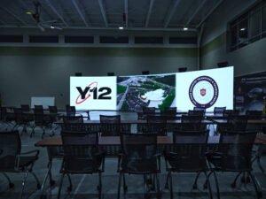 Commercial interior photograph of a massive curved LED video wall displaying Y-12 ORETTC graphics in a high-ceiling training auditorium with tiered classroom seating by Dwayne Hickson, Graphic Productions in Oak Ridge, TN.