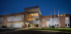 Twilight architectural photograph of the Emergency Response Training Facility at ORETTC showing illuminated glass atrium, exterior metal panels, and flagpoles by Dwayne Hickson, Graphic Productions in Oak Ridge, TN.