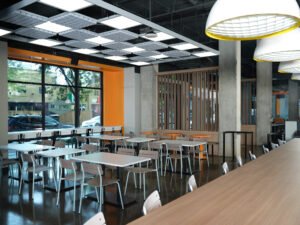 Wide view of the University of Tennessee Cumberland Food Hall dining area with geometric acoustic ceiling panels, wood slat divider, and polished concrete floors in Knoxville, TN.