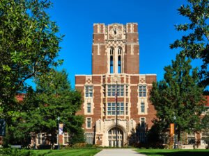 Architectural photograph of historic Ayres Hall Collegiate Gothic clock tower framed by vibrant green tree foliage on The Hill at UTK in Knoxville, TN.