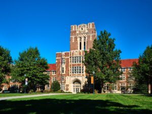 Wide exterior architectural photograph of Ayres Hall showing full brick wings, clock tower, and sunlit green lawn on The Hill at UTK in Knoxville, TN.