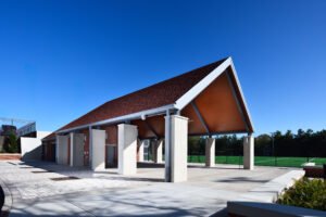 Covered open-air pavilion with concrete support columns, wood-paneled pitched ceiling, brick accents, and view of the artificial turf field at the University of Tennessee Knoxville.