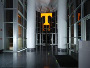 Symmetrical night view of Brenda Lawson Athletic Center lobby with glowing orange Power T sign, terrazzo floors, and round columns in Knoxville, TN.