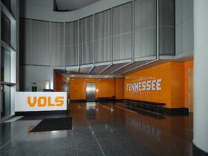 Commercial interior photograph of the Brenda Lawson Athletic Center lobby showing Vols reception desk, curved perforated metal mezzanine, and orange branding by Dwayne Hickson, Graphic Productions in Knoxville, TN.