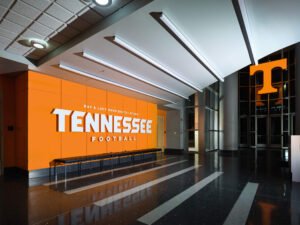 Architectural interior photograph of Brenda Lawson Athletic Center lobby showing orange Tennessee Football wall, sleek linear lighting, and terrazzo floors in Knoxville, TN.