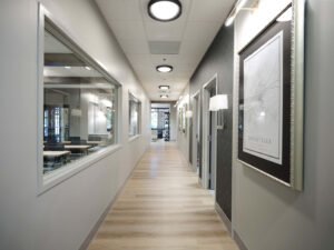 Symmetrical commercial interior photograph of an empty corporate hallway with luxury vinyl wood flooring, interior glass observation windows, and modern lighting by Dwayne Hickson, Graphic Productions in Knoxville, TN.
