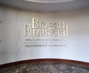 Architectural interior photograph of brushed champagne gold dimensional wall lettering for Brogan Financial mounted on a curved textured wall with polished marble tile flooring by Dwayne Hickson, Graphic Productions in Knoxville, TN.
