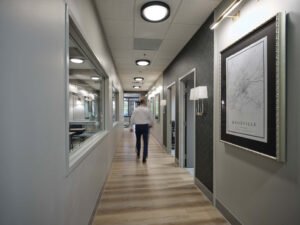 Commercial interior photograph of a modern office hallway with motion blur professional walking, wood-look flooring, geometric accent wall, and wall sconces by Dwayne Hickson, Graphic Productions in Knoxville, TN.