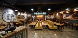 Panoramic commercial interior photograph of Buffalo Breakfast Company showing distressed brick walls with painted buffalo mural, concrete floors, wood dining tables, and booth seating by Dwayne Hickson, Graphic Productions in Sevierville, TN.