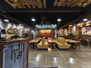Commercial interior photograph of the rustic dining room at Buffalo Breakfast Company featuring polished concrete floors, leather booth seating, corrugated metal hostess station, and Tennessee tri-star flag wall art by Dwayne Hickson, Graphic Productions in Sevierville, TN.