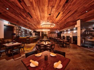 Warm architectural interior of Elkmont Station dining room with vaulted tongue-and-groove wood ceiling, wagon wheel chandelier, and full bar in Knoxville, TN.