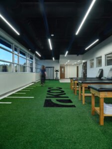 Vertical interior view of Knoxville Orthopaedic Clinic therapy room with indoor turf, treatment tables, and staff in motion