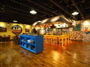 Commercial interior photograph of Over Easy Al’s Breakfast showing warm wide-plank wood floors, bright blue mobile service cart, stacked stone bar, and exposed ceiling joists by Dwayne Hickson, Graphic Productions in Gatlinburg, TN.