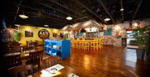 Panoramic commercial interior photograph of the open dining room at Over Easy Al’s Breakfast showing exposed ceiling trusses, wide-plank wood floors, dining tables, and tiki bar by Dwayne Hickson, Graphic Productions in Sevierville, TN.