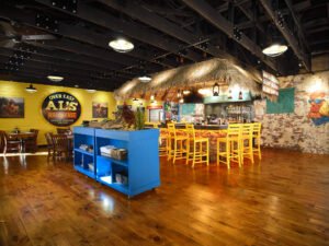 Master light-painted commercial interior photograph of Over Easy Al’s Breakfast featuring illuminated stone tiki bar, yellow barstools, blue service island, and rustic wood floors by Dwayne Hickson, Graphic Productions in Gatlinburg, TN.