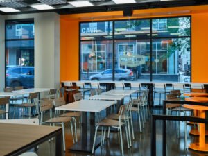 Modern dining area at UTK Cumberland Food Hall with polished floors, orange accent wall, and window seating in Knoxville, TN.