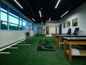 Physical therapy rehabilitation room at KOC Surgery Center featuring indoor turf, treatment tables, and motion blur figure by Johnson Architecture in Knoxville, TN.