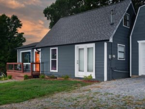 Angled dusk architectural photograph of a modern blue lakehouse vacation rental with steep gabled roofline, front porch deck, and sunset sky by Dwayne Hickson, Graphic Productions in Dandridge, TN.
