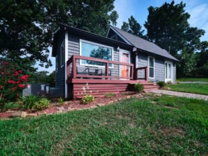 Low-angle exterior architectural photograph of a blue lakefront vacation rental cottage with red front porch deck, flowering landscape, and green lawn by Dwayne Hickson, Graphic Productions in Dandridge, TN.