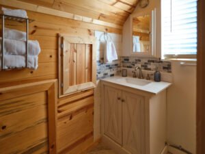 Rustic cabin bathroom featuring a single white vanity, slate-look tile backsplash, mirrored medicine cabinet, and natural pine tongue-and-groove walls.