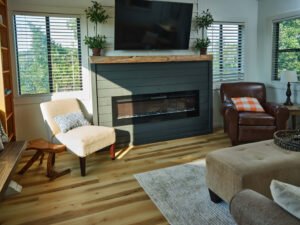 Interior architectural photograph of a bright Douglas Lake vacation rental living room featuring light hardwood floors, modern shiplap fireplace with live-edge mantel, and cozy seating by Dwayne Hickson, Graphic Productions in Dandridge, TN.