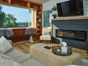 Douglas Lake vacation rental living room featuring an electric fireplace, live-edge wood mantel, and lakeview picture window seat.