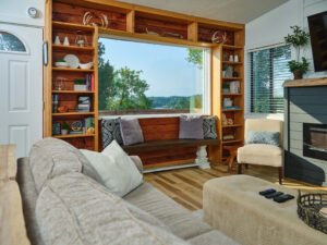Interior architectural photograph of a bright lakehouse vacation rental living room featuring custom wood built-in bookshelves framing an oversized picture window with lake views, window bench, and sofa by Dwayne Hickson, Graphic Productions in Dandridge, TN.