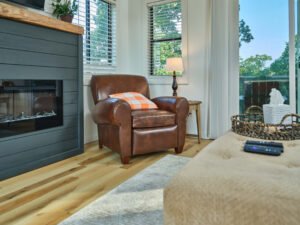 Interior architectural vignette of a Douglas Lake vacation rental living room featuring a brown leather armchair beside a dark shiplap fireplace, bedside lamp, and sliding glass deck door by Dwayne Hickson, Graphic Productions in Dandridge, TN.